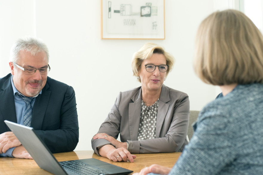 Sven Fiedler, Ute Zemann-Zipser, Timo Riegel und Dr. Anne Schäfer sitzen an einem Tisch um einen Laptop versammelt. Sie sind im Gespräch.